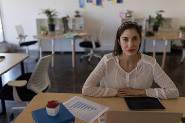 Businesswoman in office sitting at desk with tablet and financial charts, copy space