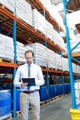 Businessman in warehouse checking inventory on clipboard, surrounded by shelves, copy space