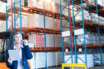 Businesswoman using tablet and talking on phone in large warehouse, copy space