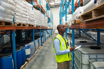 Warehouse worker in safety vest inspecting inventory on shelves with clipboard, copy space