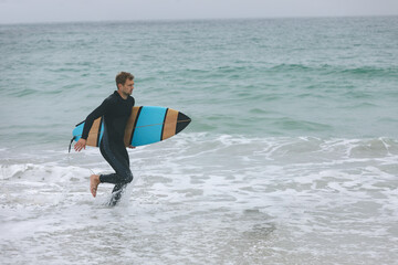 Surfer carrying board running into ocean, preparing for exciting surf session, copy space