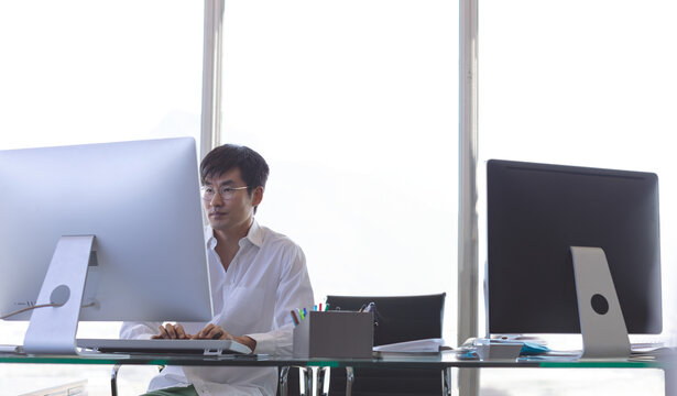 Asian man working on desktop computer in modern office, focusing on task, copy space