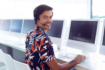 Customer service representative smiling while using headset at computer in office, copy space