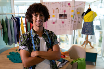 Fashion designer smiling confidently in creative studio with clothing and sketches, copy space