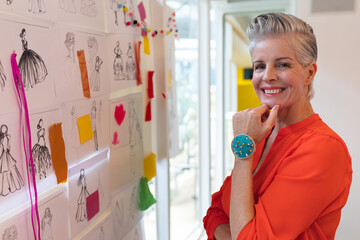In office, fashion designer smiling confidently surrounded by sketches and fabric swatches, copy spa