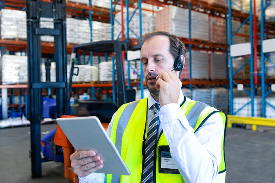 Using tablet and headset, warehouse manager managing inventory and communicating