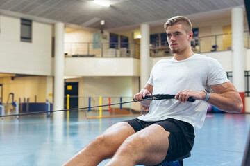 Focused man using rowing machine in sports center, building strength and endurance, copy space