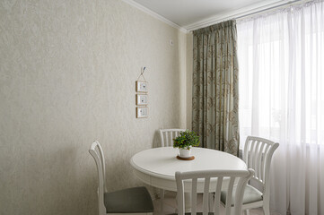 Cozy dining area with a white round table and chairs. Neutral wall with framed pictures and window with curtains