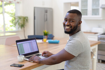 African American man working on laptop at home, smiling and enjoying coffee