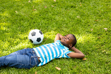 On grass, African American child smiling with soccer ball, relaxing outdoors