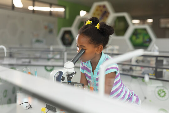 In school science lab, African American girl using microscope, exploring with curiosity, copy space