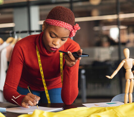 Recording voice note while sketching, African American woman in fashion studio