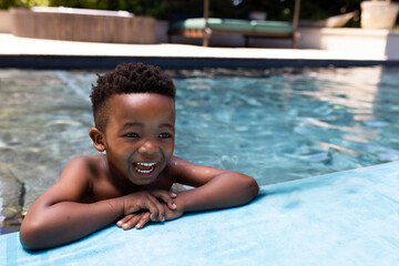 Smiling African American boy enjoying swimming in pool on sunny day