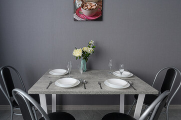 gray table set with white plates, silverware, and glasses, a vase of flowers, and four chairs