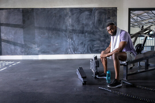 African American man resting on gym bench with towel and water bottle, copy space - Powered by Adobe