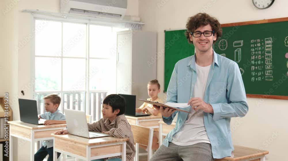 Poster caucasian teacher checking document and looking at camera at classroom. diverse children sitting at 