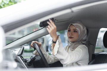 Muslim women adjusting rearview mirror while sitting in driver seat, showing safe driving awareness, responsibility, and confidence in modern transportation lifestyle