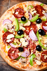 Pizza with chorizo ​​sausage, mozzarella cheese, green pepper and black olives. Rustic wooden background. Soft focus.	