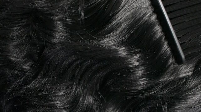 Closeup black hair texture, slow motion of female hand combing long curly hair
