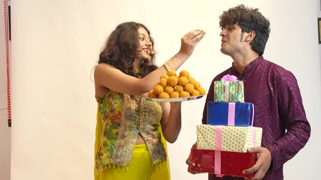 Young indian brother and sister celebrate rakshabandhan or Diwali festival enjoy eating laddu or laddoo sweet with gift boxes isolated on white background.4K