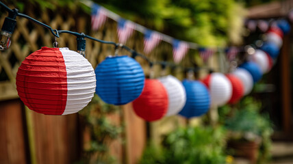 Fototapeta premium A photo of red, white, and blue paper lanterns hanging from an outdoor string light in front of a garden fence. Ai generated
