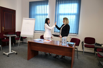 Women in business suits exchange a high five gesture, celebrating a team victory.