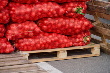 Large red mesh bags filled with onions stacked on wooden pallets at rural wholesale market, farm harvest ready for trade. Photo