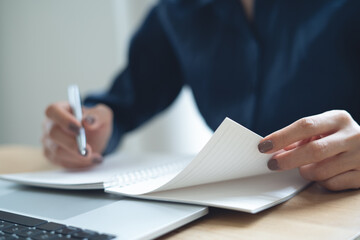 Close up of business woman hand writing on notebook at office with laptop computer on table. Student studying online class and taking note in notepad, e-learning