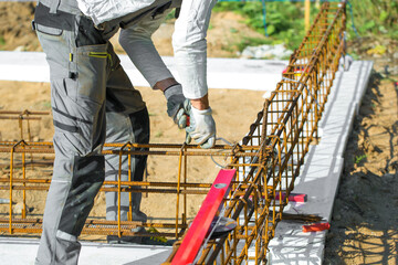 
Close-up of worker's hands in gloves, who is tying reinforcement for foundation reinforcement.
