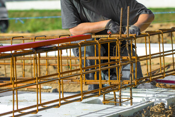 
Close-up of worker's hands in gloves, who is tying reinforcement for foundation reinforcement.
