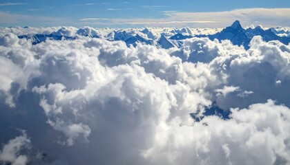 Fototapeta premium A breathtaking vista of snow-capped mountain peaks piercing through a dense field of puffy white clouds, viewed from an elevated perspective.