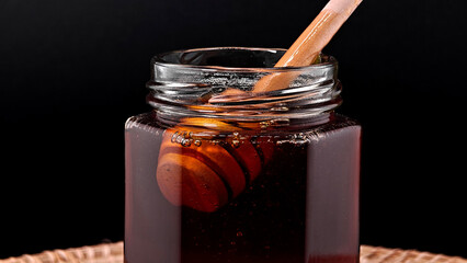 Wooden Honey Dipper in Honey Jar on Black Background.