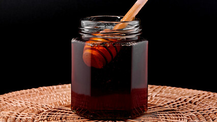 Wooden Honey Dipper in Honey Jar on Black Background.