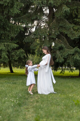 Fototapeta premium A pregnant woman and her little daughter are dancing outdoors in a park. The woman and the little girl are having fun together, holding hands.