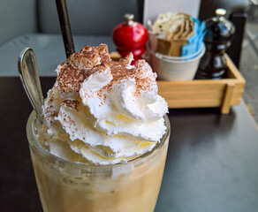 Iced caramel latte coffee in a tall glass with whipped cream on black table.