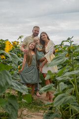 Fototapeta premium A family with two daughters in a sunflower field, looking at the camera. Concept of growing crops, agriculture, farming, autumn, harvesting