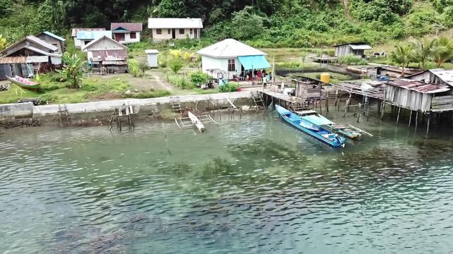 Traditional coastal village with wooden houses, fishing boats, and residents near the shore, showing daily rural life by the sea in a tropical island community.