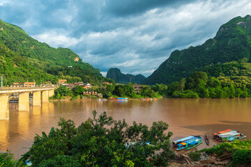 Houses and traditional Laotian wooden slow boat on Nam Ou river near Nong Khiaw village, Laos.