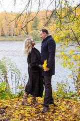 A woman and man looking at each other by the river covered with fallen autumn leaves for autumn season