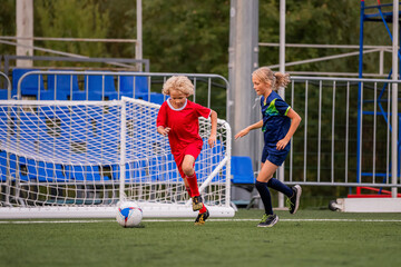 Boy and girl children playing football on a green field.