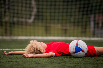 Little boy in football uniform lying down exhausted on soccer field