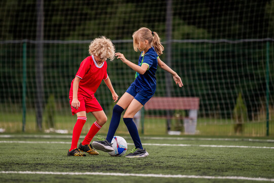 Boy and girl children playing football on a green field.