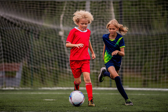 Boy and girl children playing football on a green field.