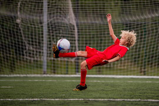 young boy performing bicycle kick with football on green field.