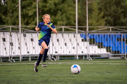 girl soccer player runs on field with ball during training or game.