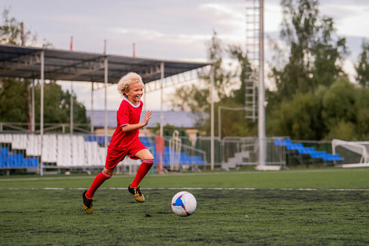 boy with curly hair runs with a football on a green field.