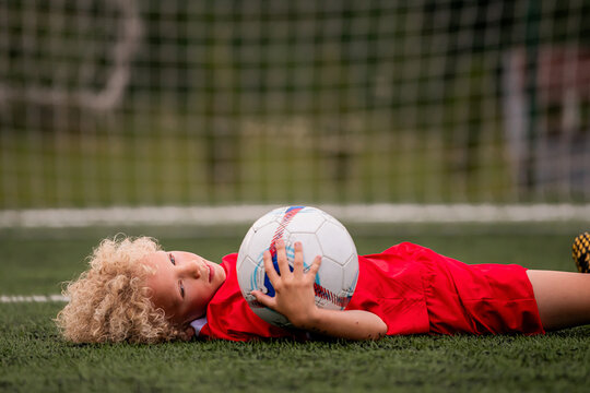 Little boy in football uniform lying down exhausted on soccer field
