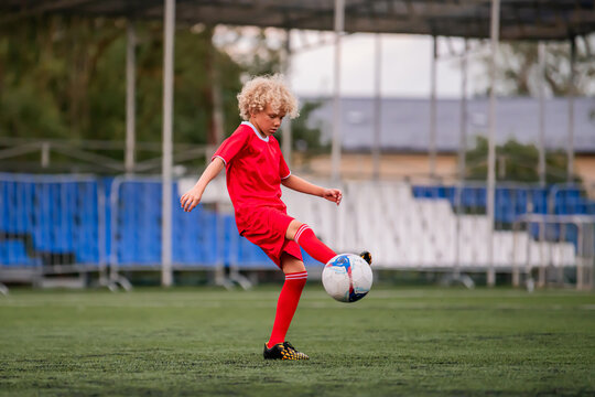 boy with curly hair runs with a football on a green field.