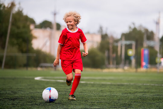 boy with curly hair runs with a football on a green field.