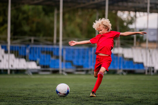boy with curly hair runs with a football on a green field.